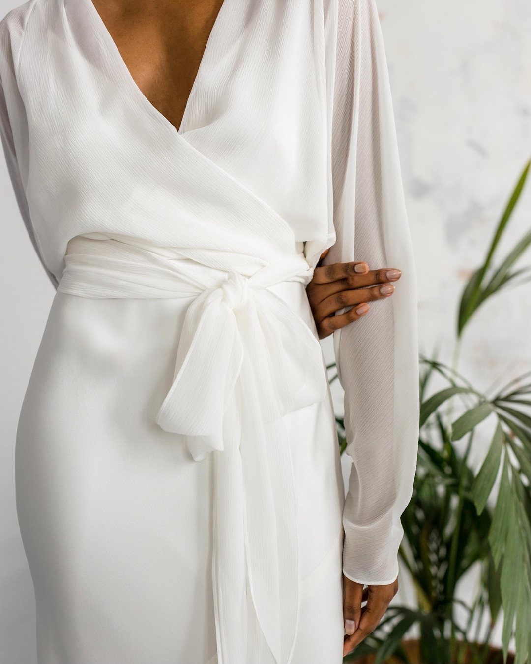 White wrap wedding dress with sheer long sleeves and a tied waist sash.