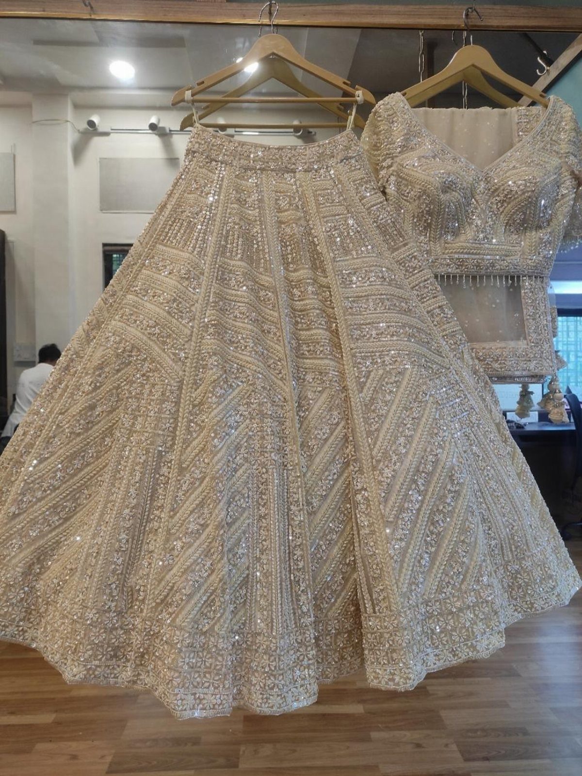 Off-white bridal lehenga with intricate shimmering embroidery hanging on wooden hangers.