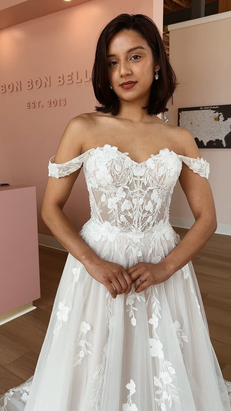 Woman wearing an off-white wedding dress with floral lace and off-the-shoulder straps.
