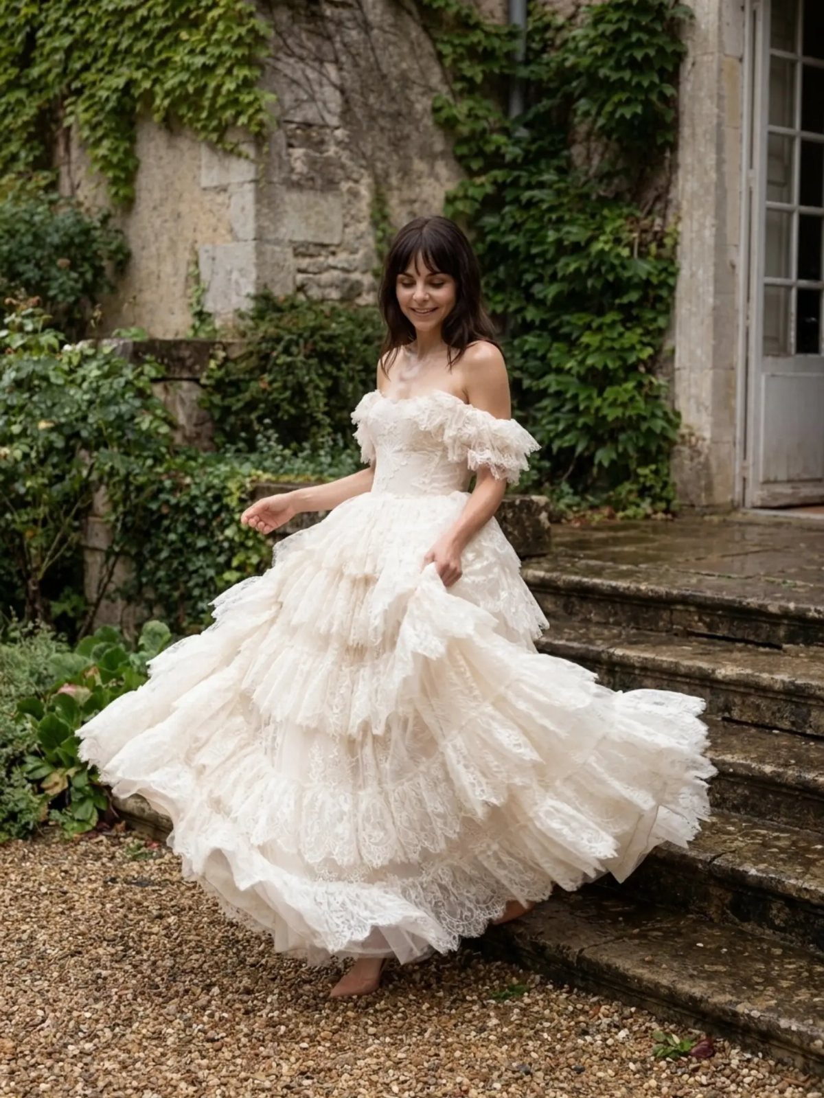 Woman in a ruffled white lace wedding dress standing on stone garden steps