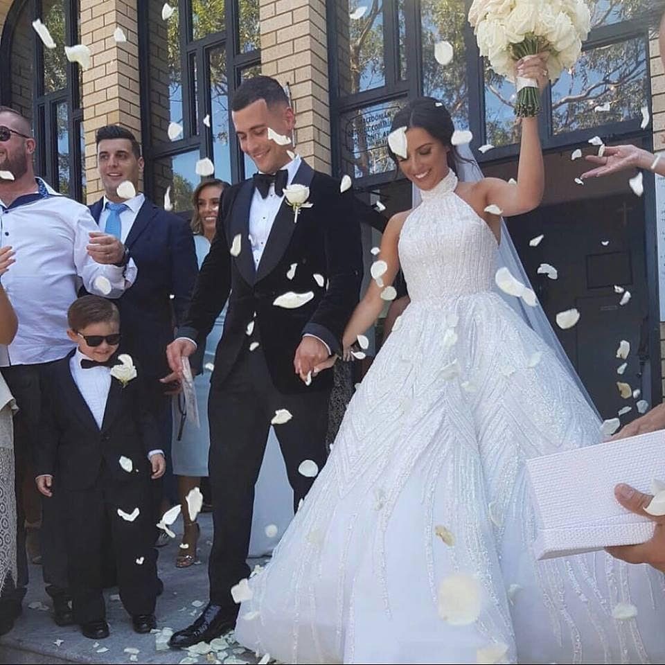 Bride in a high-necked halter wedding gown and groom walking through falling petals.