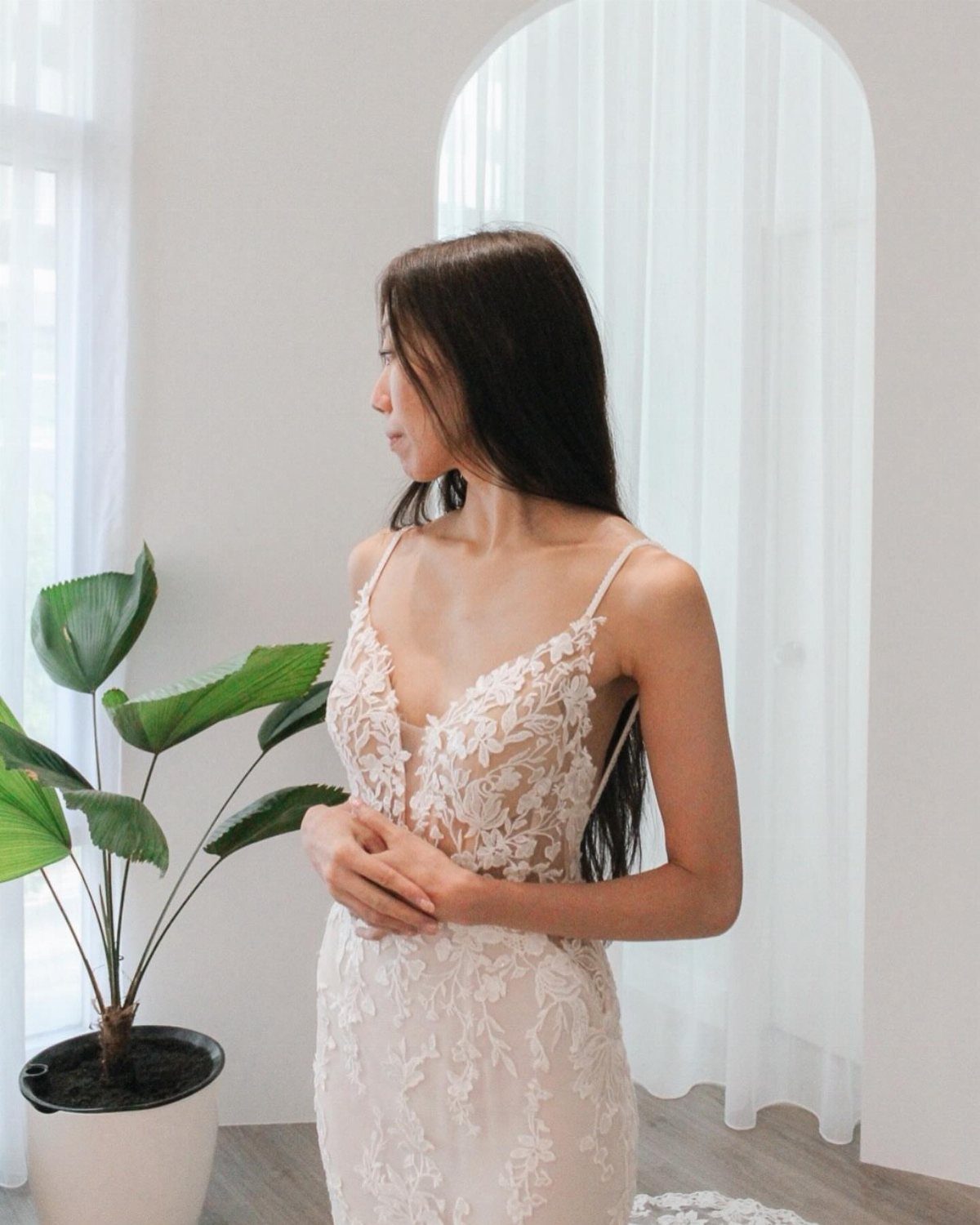 Woman wearing a white lace wedding dress with a plunging V-neckline indoors.