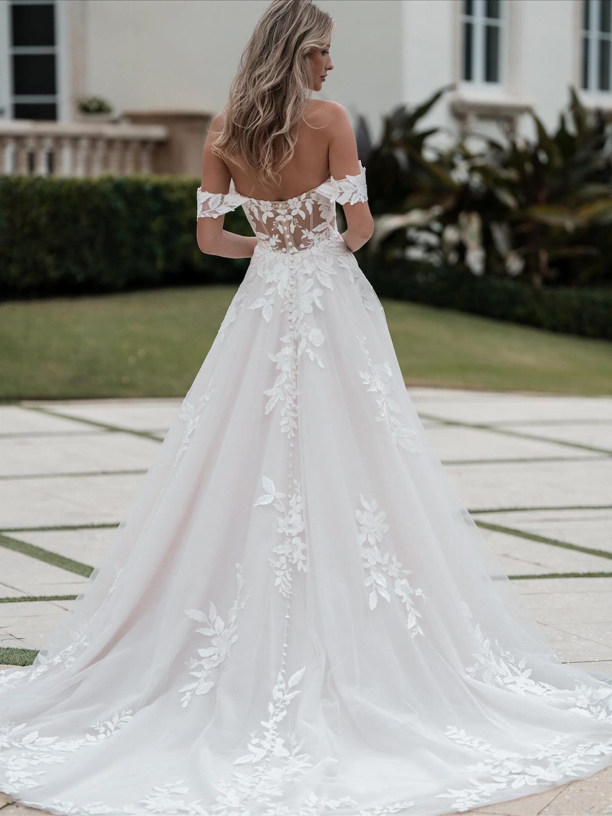 Woman in white off-the-shoulder wedding gown with lace details standing on a patio