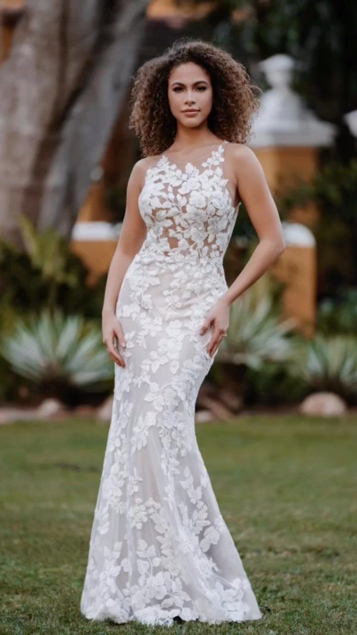 Woman wearing a white lace sheath wedding dress standing on a green lawn