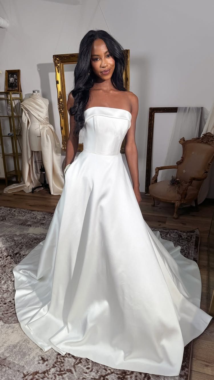 Woman in a simple strapless white satin wedding gown standing in a studio