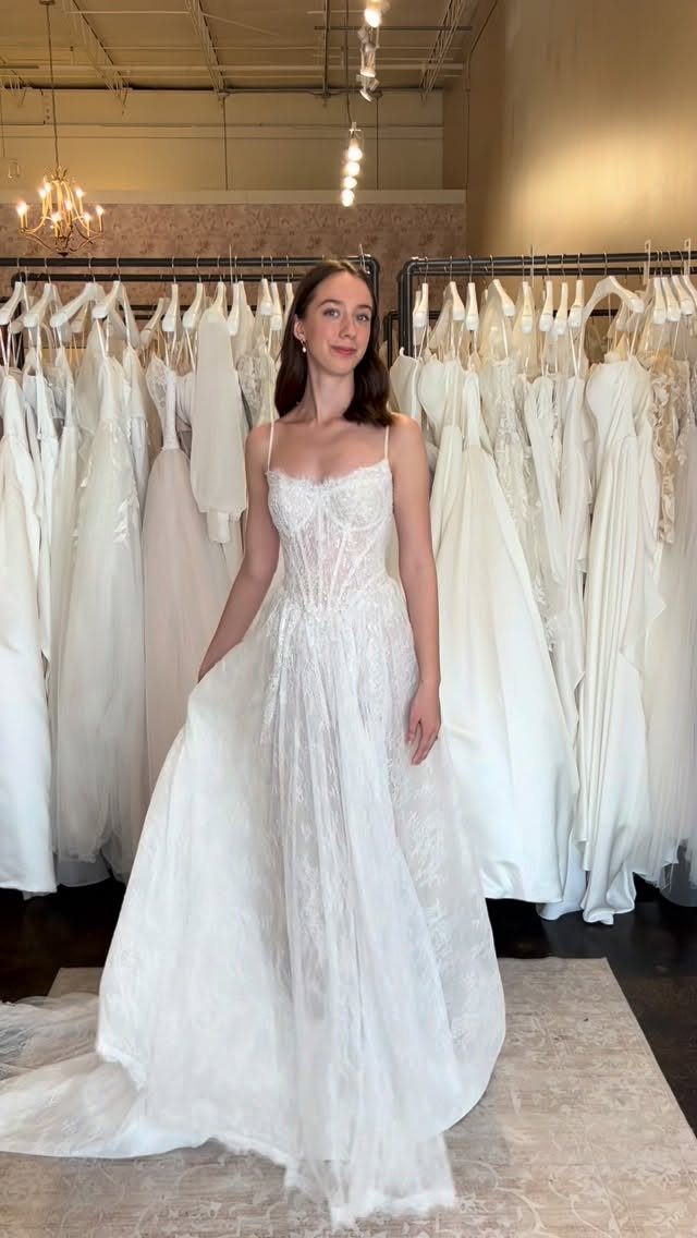 Woman wearing a white lace wedding dress standing in a bridal boutique shop