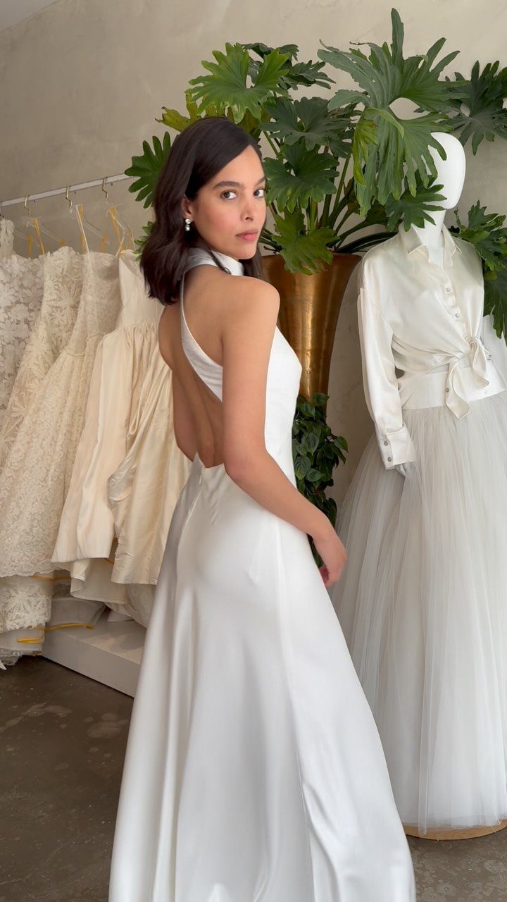 Woman in a white halter maxi wedding dress posing in a bridal boutique.
