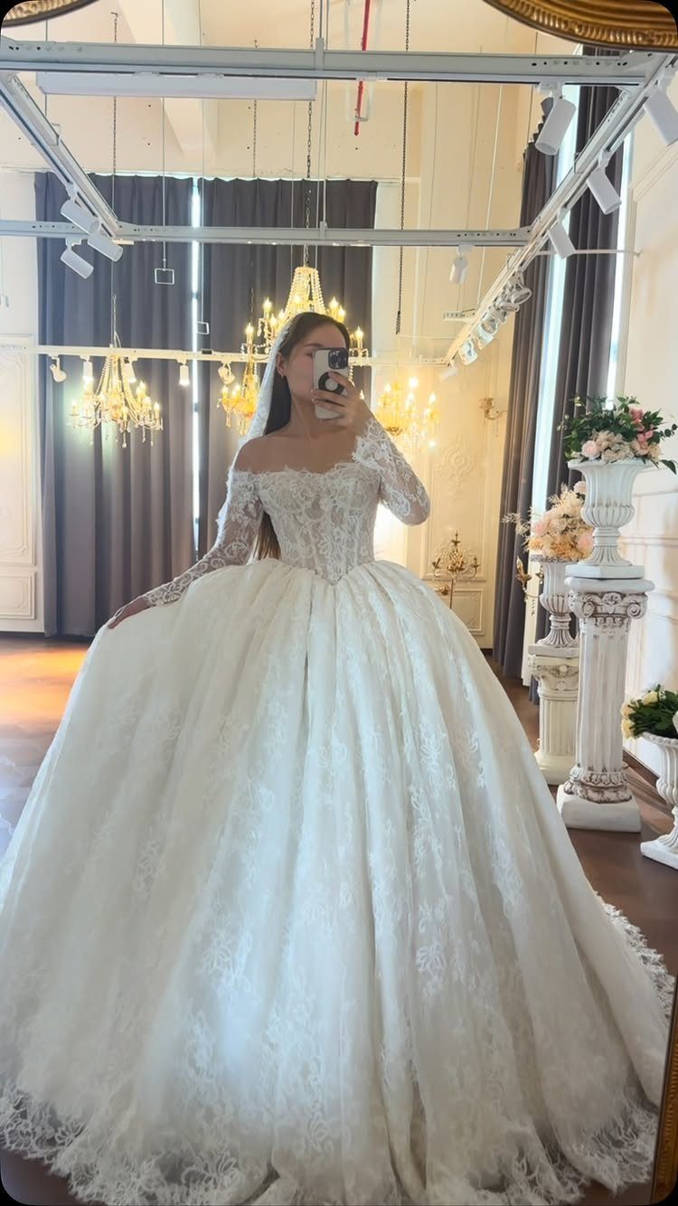 Woman in a voluminous white lace ballgown wedding dress with off-the-shoulder sleeves.
