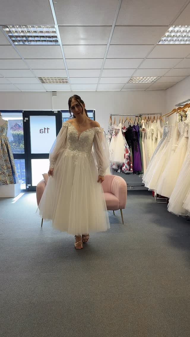 Woman in a white long-sleeved tea-length wedding dress with a full tulle skirt.