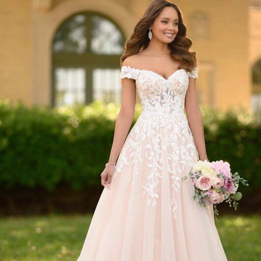 Woman in an off-the-shoulder lace wedding dress holding a pink floral bouquet outdoors