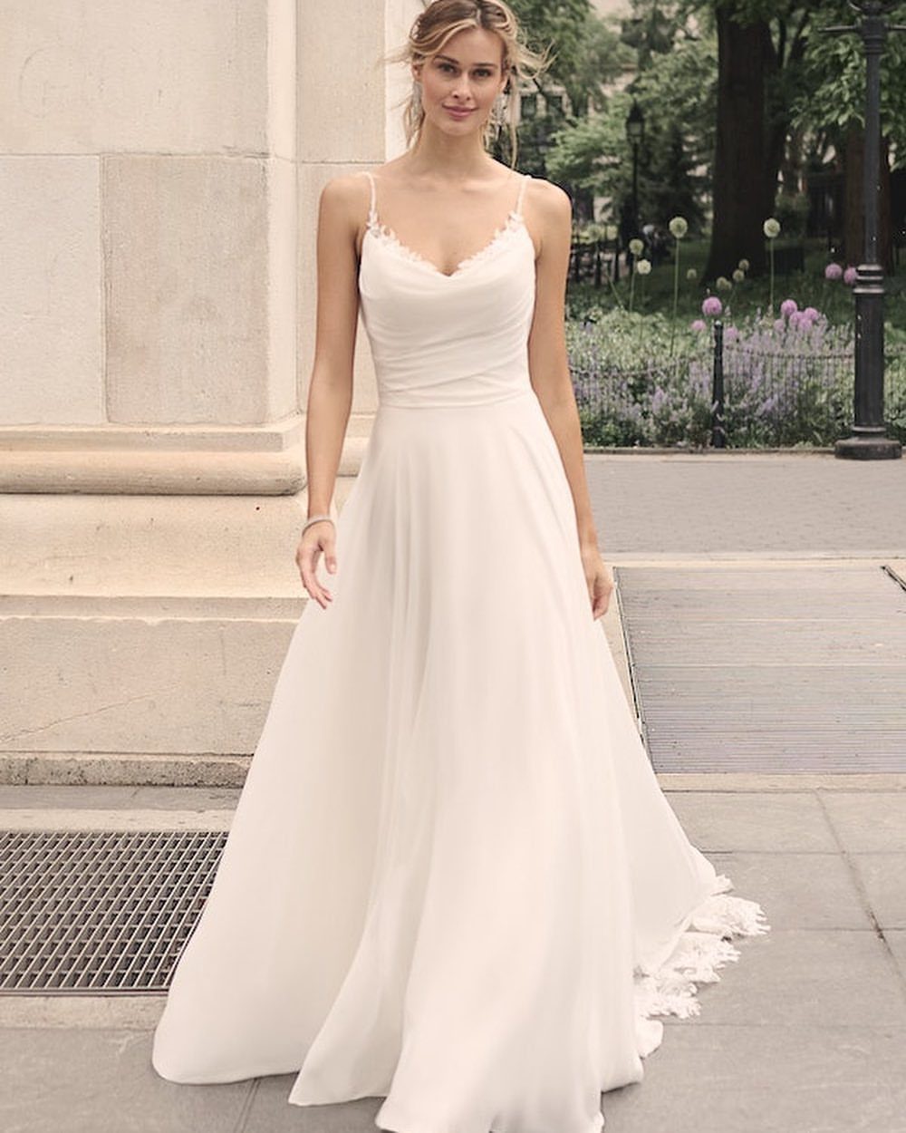Woman in a flowing off-white chiffon A-line wedding dress with thin spaghetti straps.
