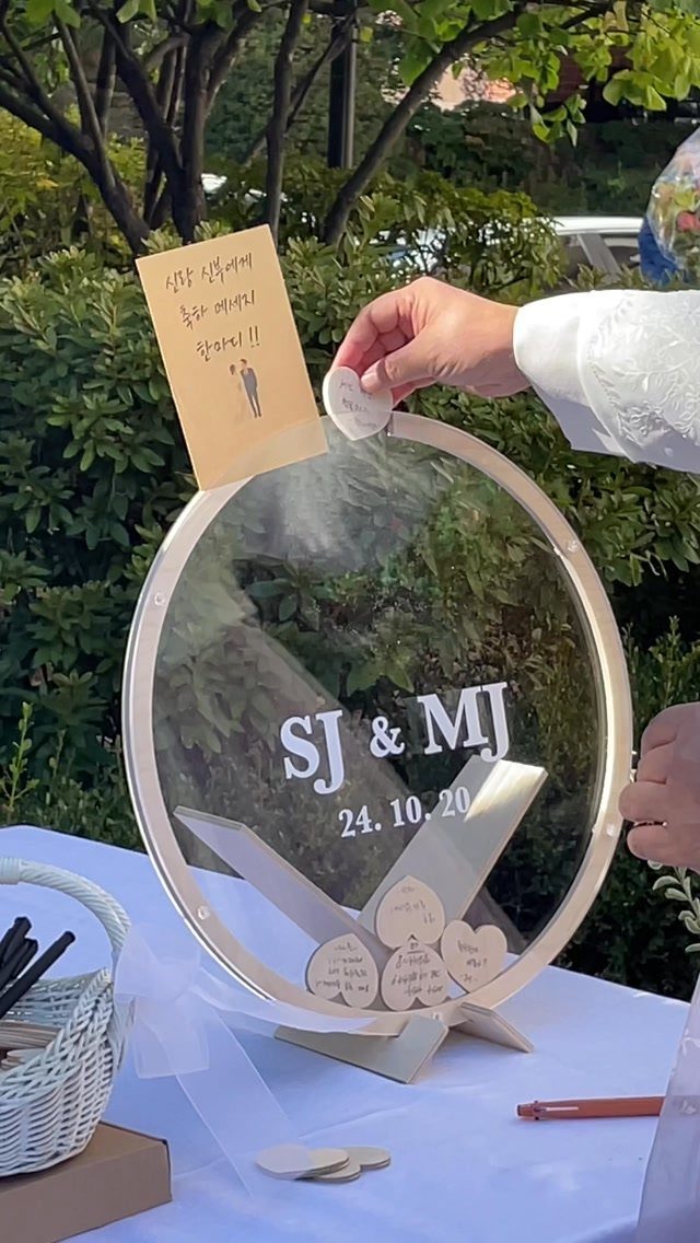 Circular acrylic guest book frame with heart tokens on a white wedding table.