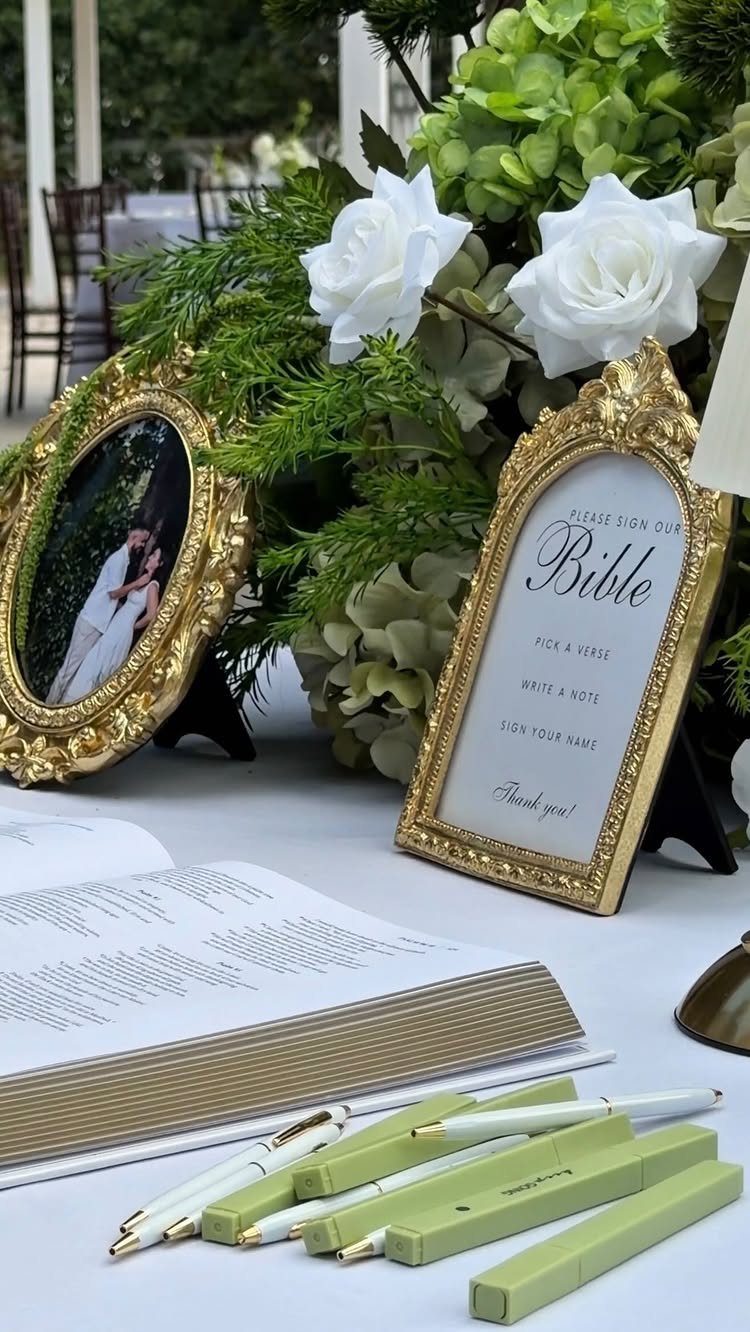 Wedding guest book table with an open Bible, gold frames, and white flowers.