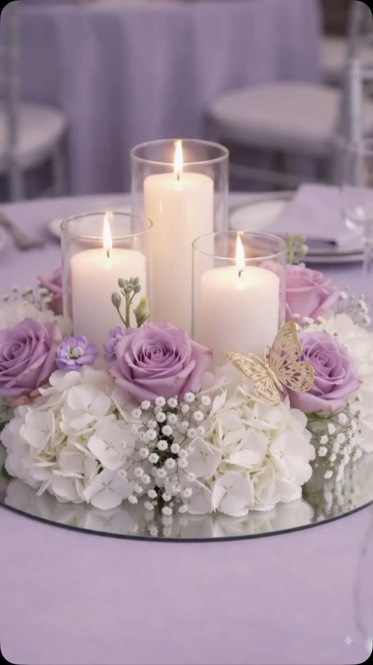 Floral arrangement with purple roses and white hydrangeas surrounding three lit pillar candles.