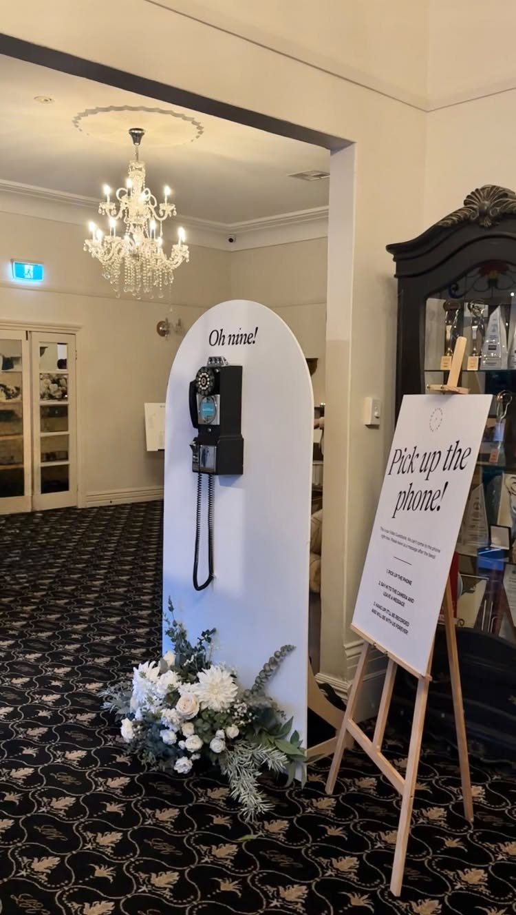 Vintage black telephone on a white arched backdrop with a nearby instructional sign.