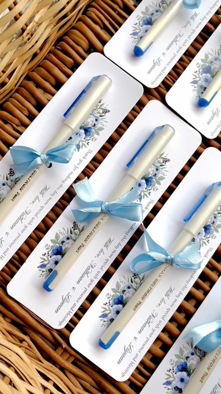 White pens with blue ribbons on floral cards resting on a wicker background.