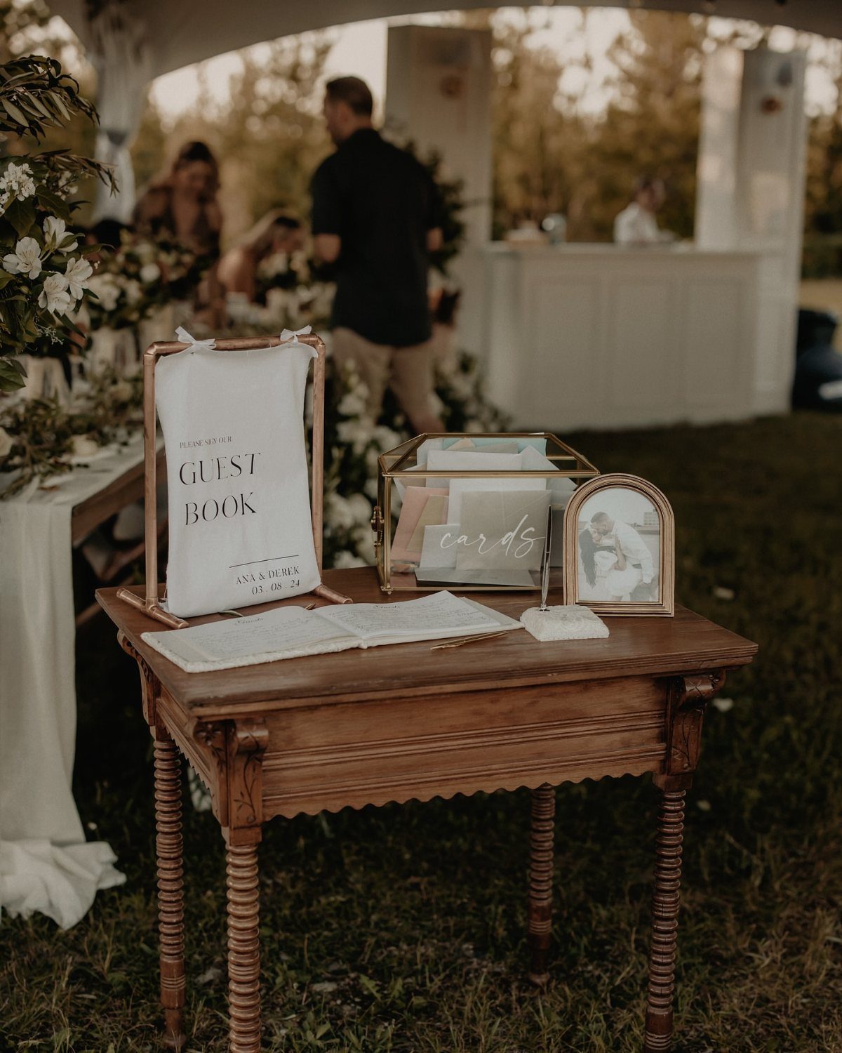 Wooden vintage table with a guest book, sign, and card box outdoors.