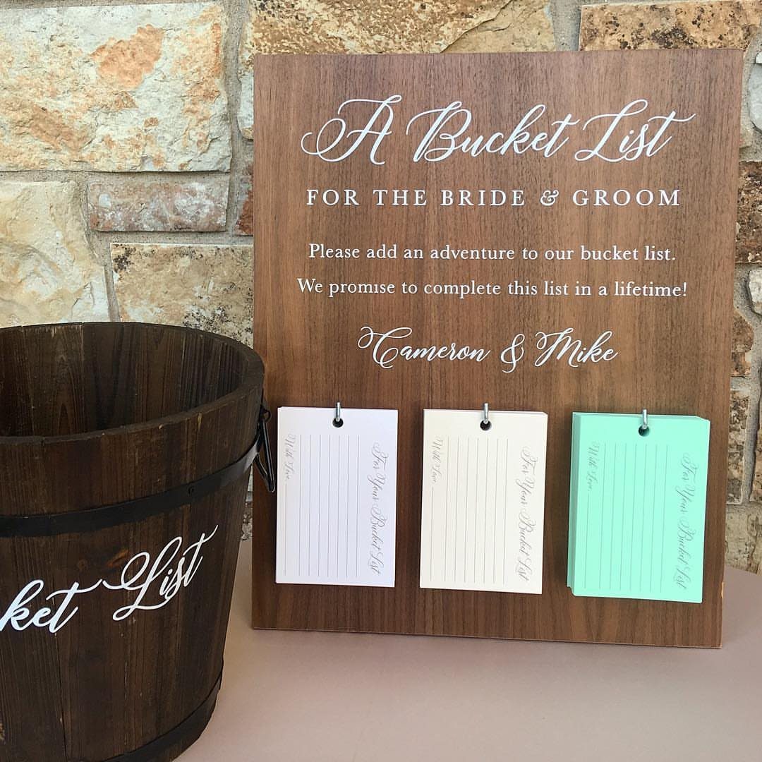 Wooden bucket list guest book sign with hanging slips of paper and wooden bucket.
