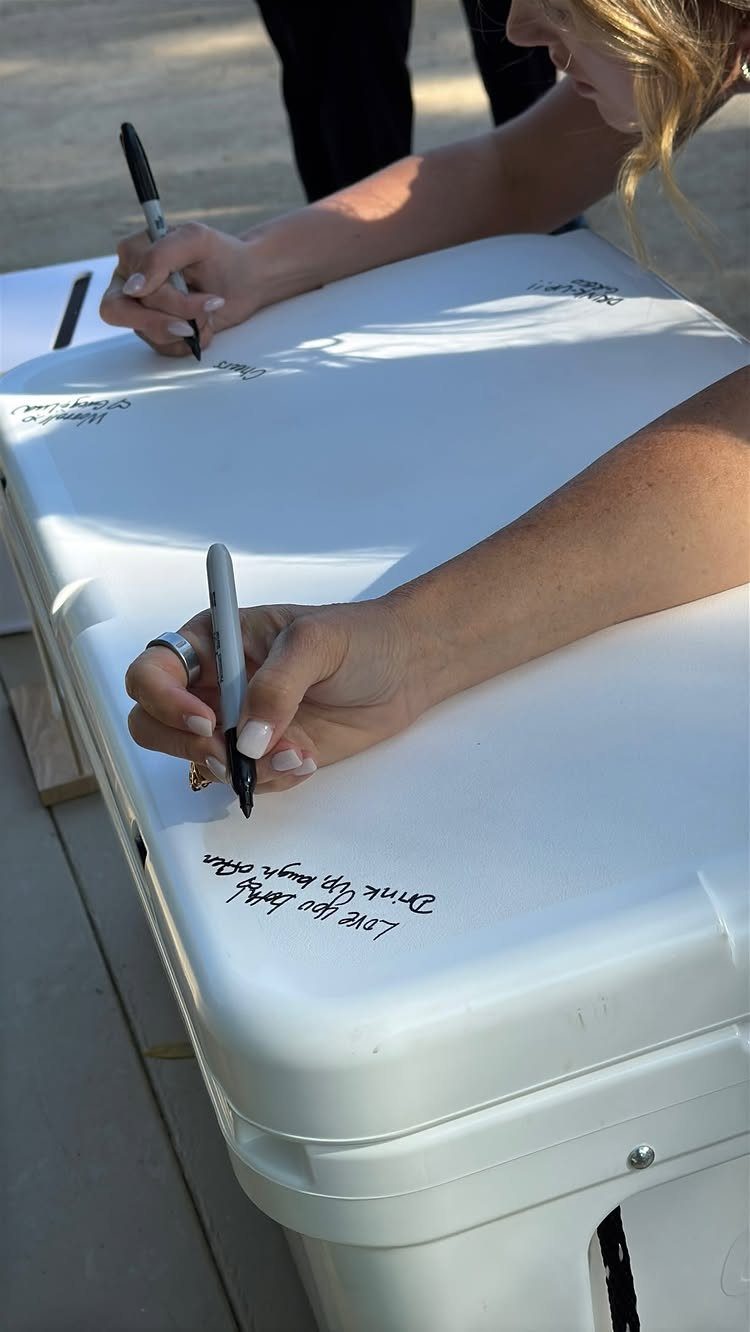 People writing messages with black markers on a white plastic cooler lid.