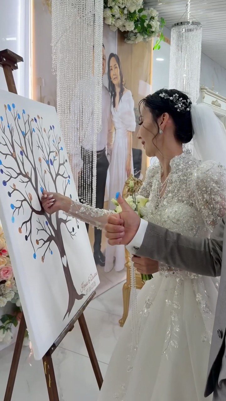 Bride adding a blue fingerprint to a tree painting on a wooden easel