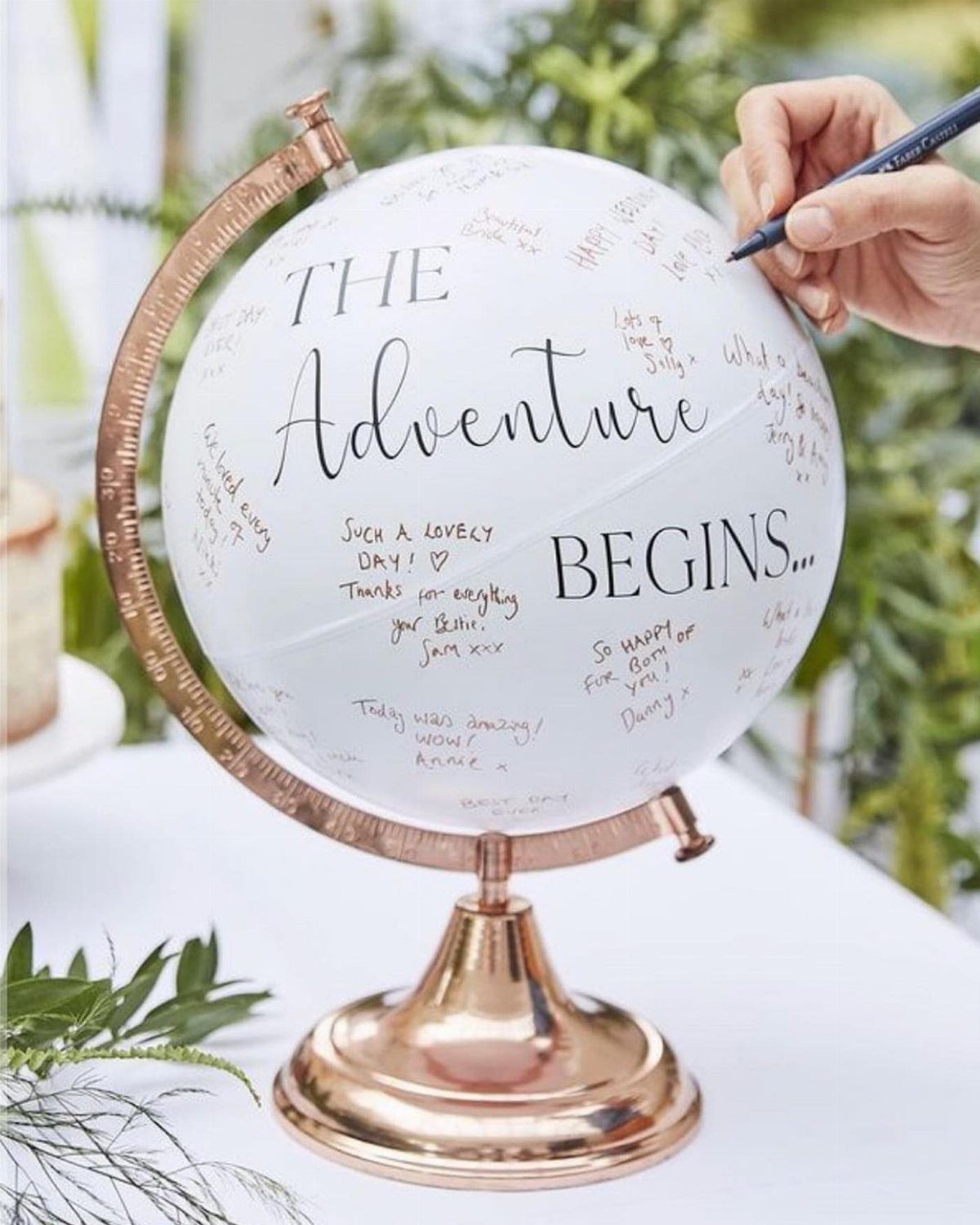 White globe guest book on rose gold stand with handwritten messages and a pen