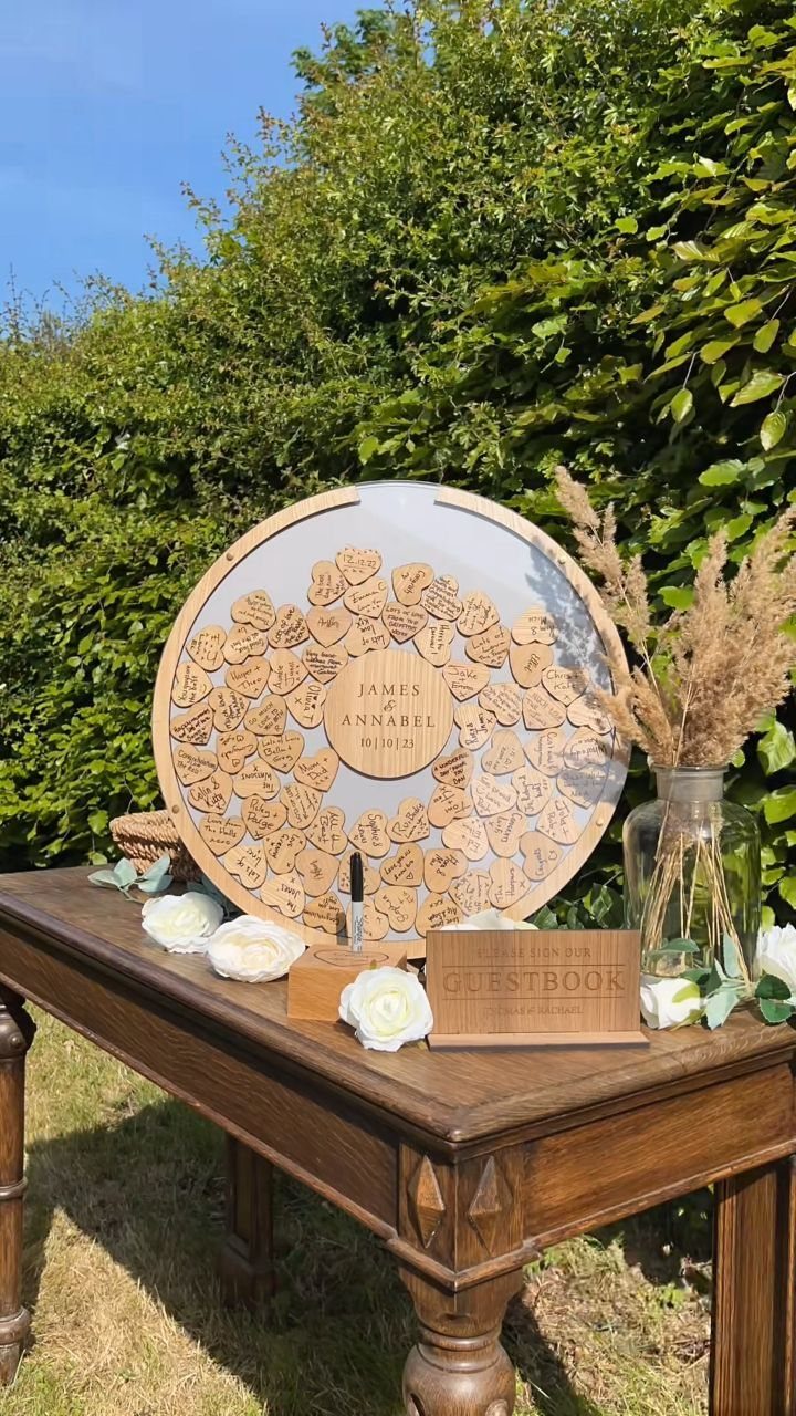 Circular wooden guest book with heart tokens on a table with white roses.