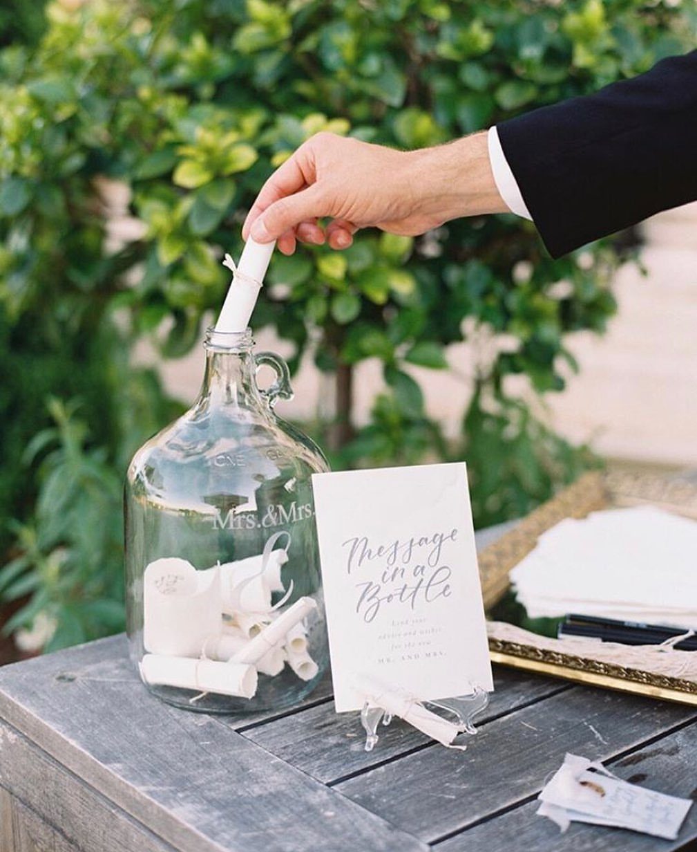 Hand placing a rolled note into a glass bottle for a wedding guest book