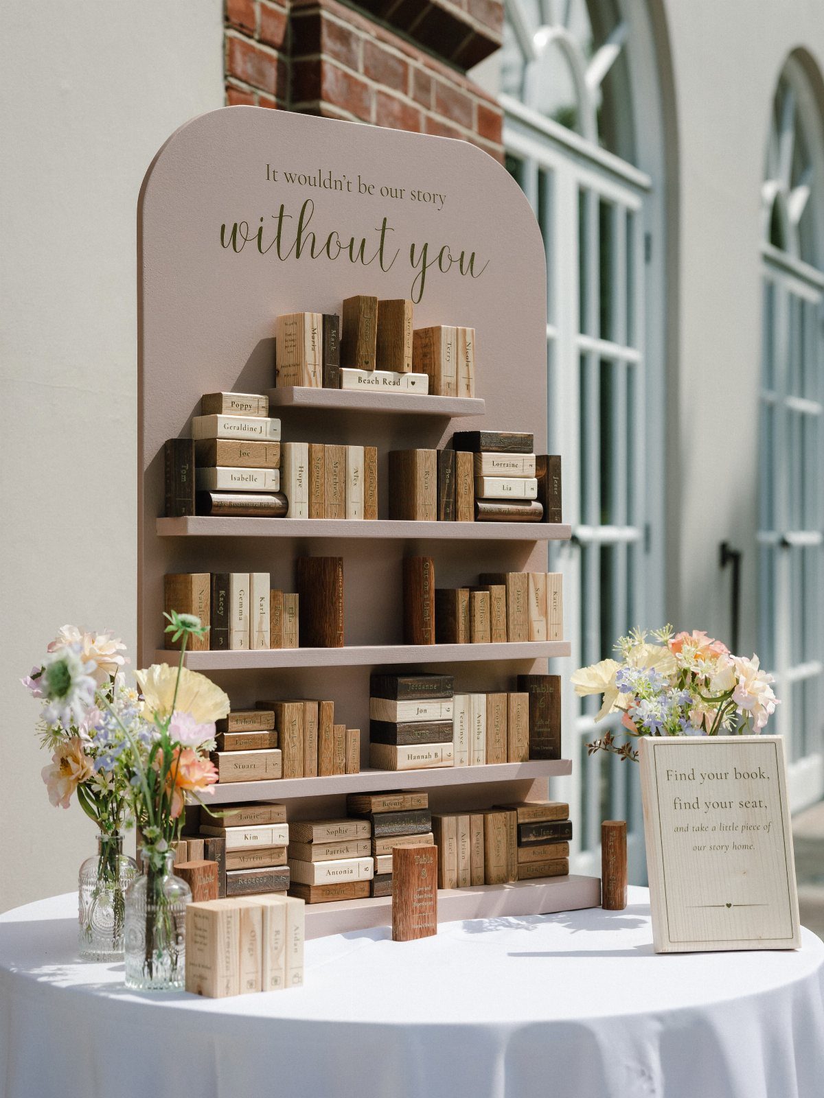 Wooden bookshelf guest book display with small book-shaped blocks and floral arrangements.