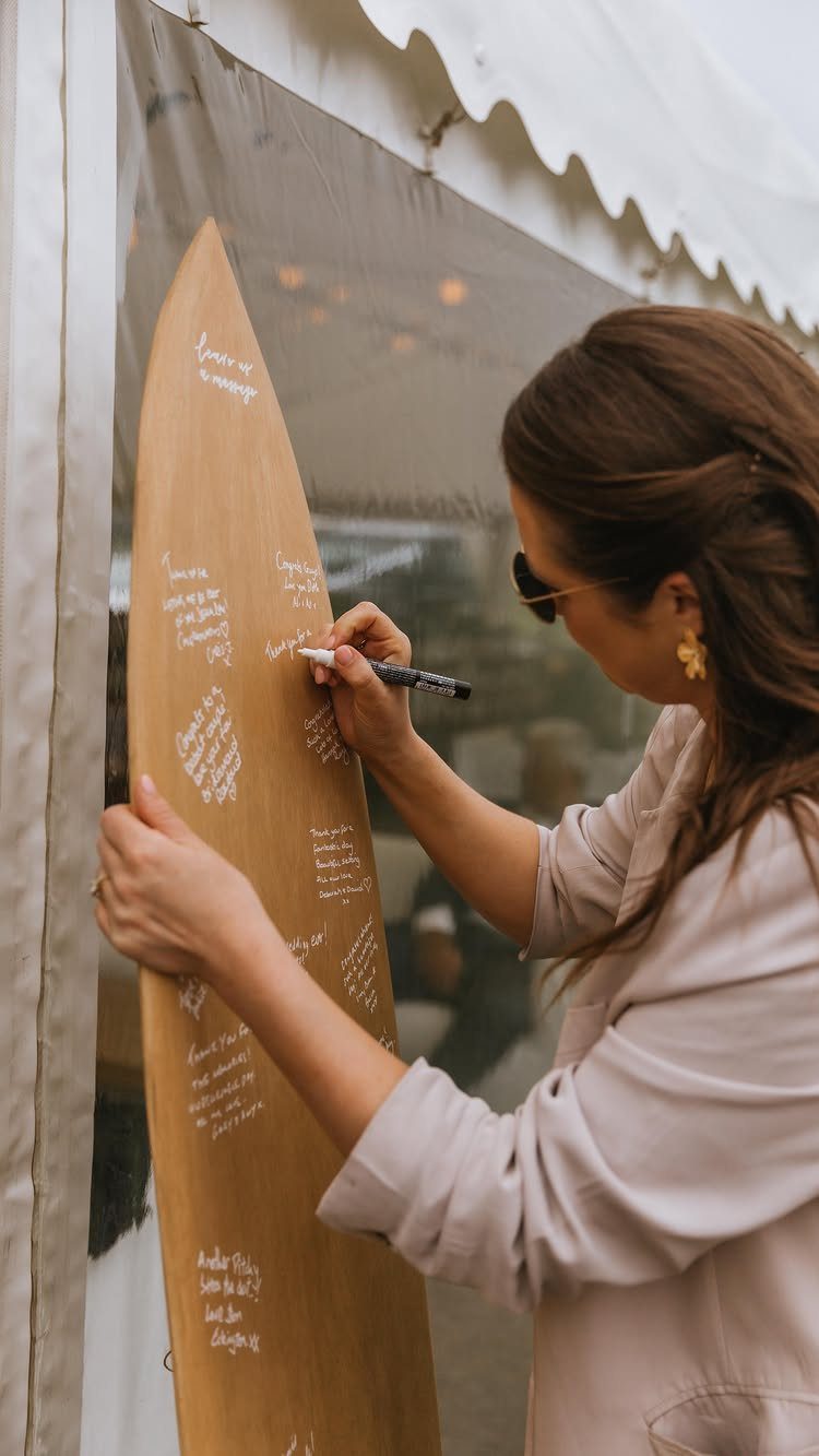 Woman writing a message on a wooden snowboard used as a wedding guest book.