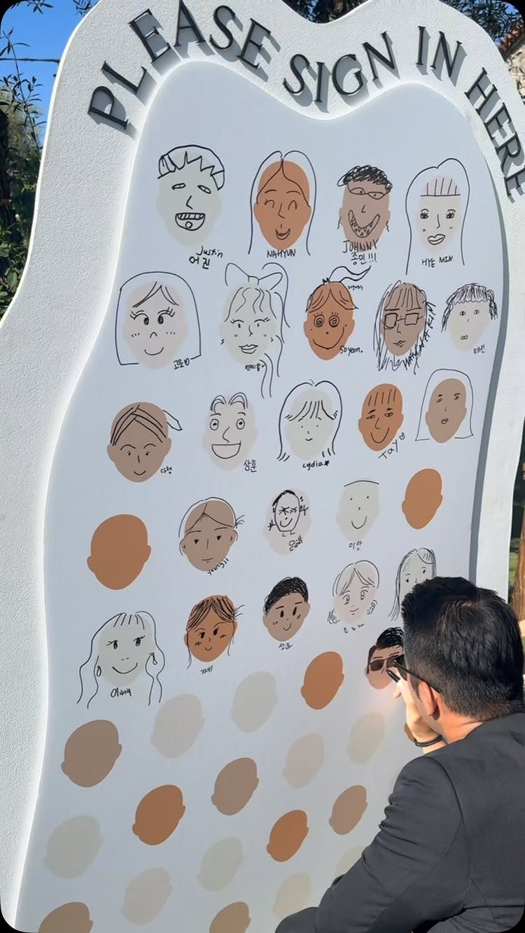 Man signing a large white art board featuring hand-drawn guest portraits and names.