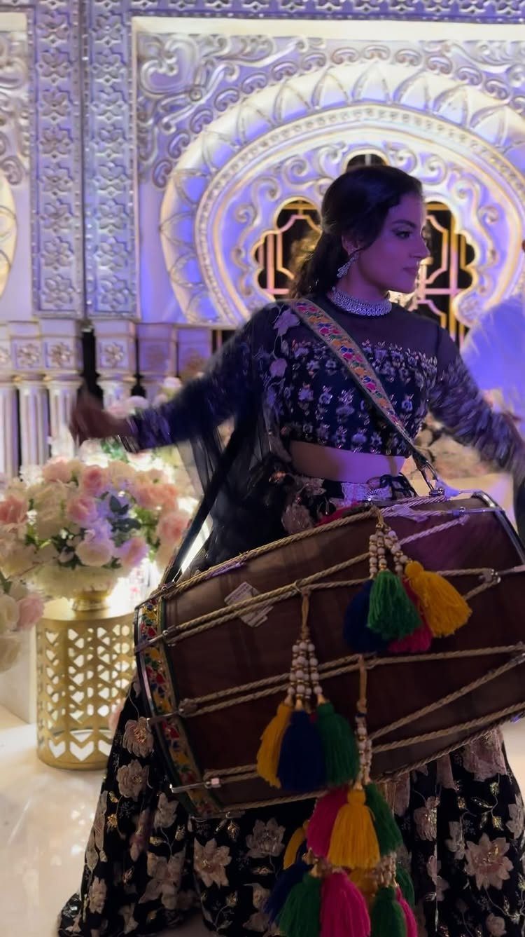 Woman in traditional Indian attire playing a dhol drum with colorful tassels.