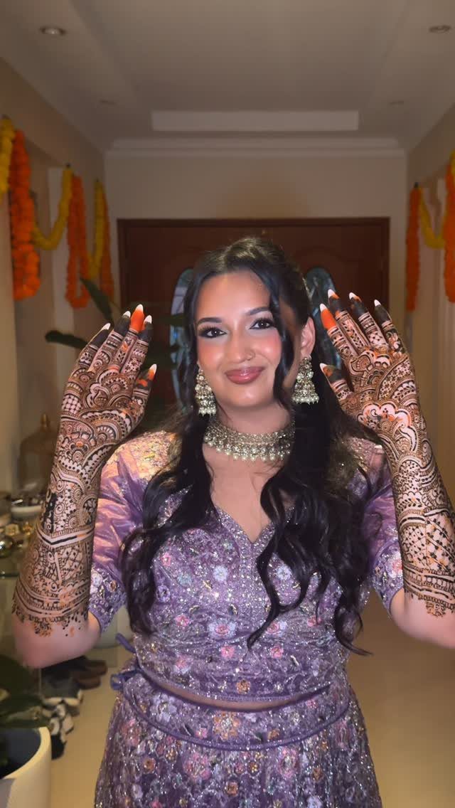 Woman in purple traditional Indian dress showing intricate henna patterns on her hands.