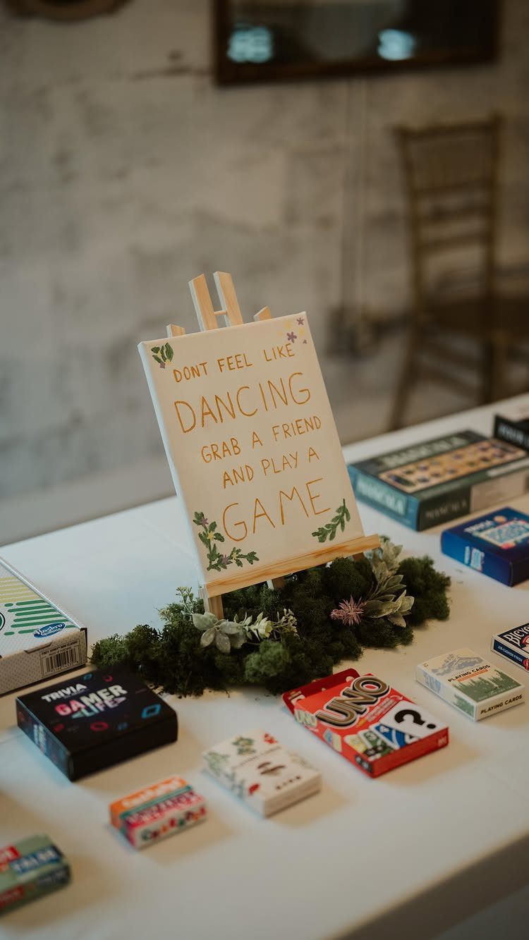 Board games and a sign inviting guests to play games on a white table.