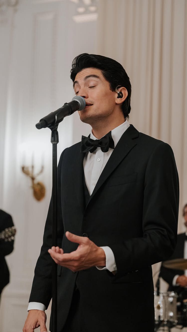 Male singer in a black tuxedo performing with a microphone at a wedding event