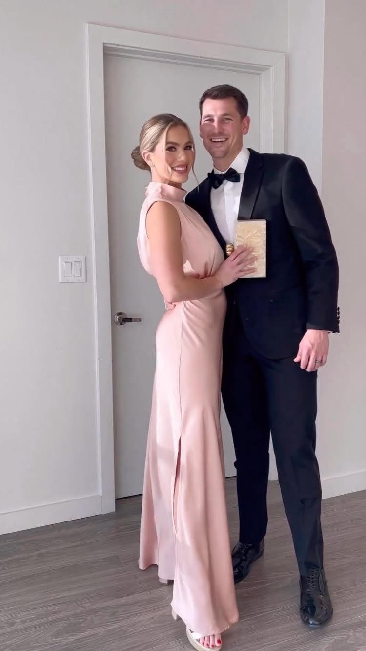 Couple posing in formal wear, woman in a floor-length pink satin gown.