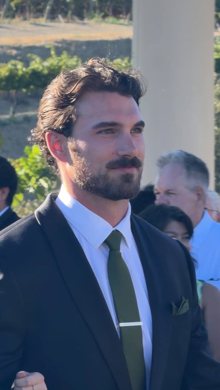 Man in a navy suit and olive green tie attending a summer wedding.