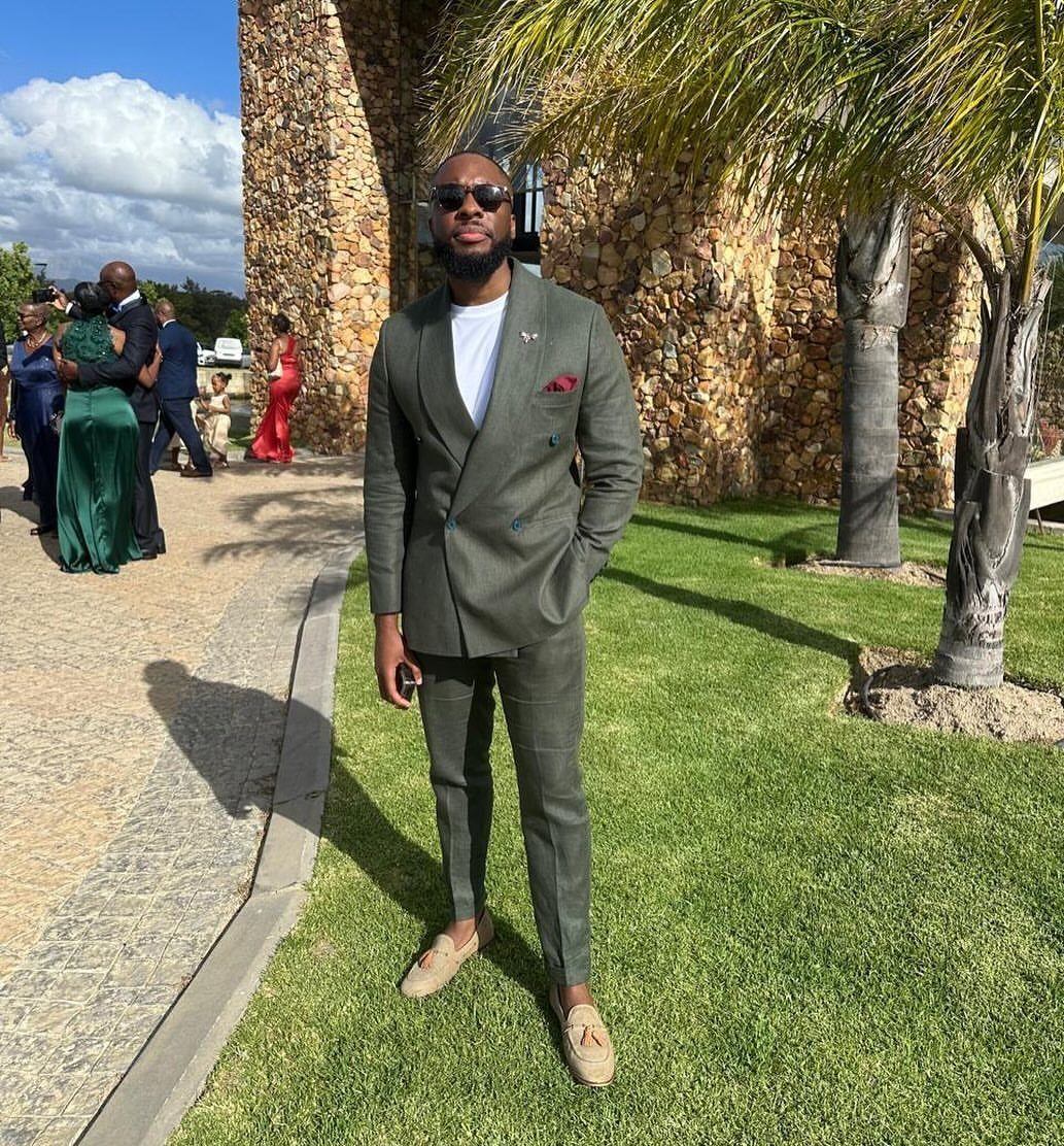 Man in olive green suit and tan loafers standing on a sunny lawn