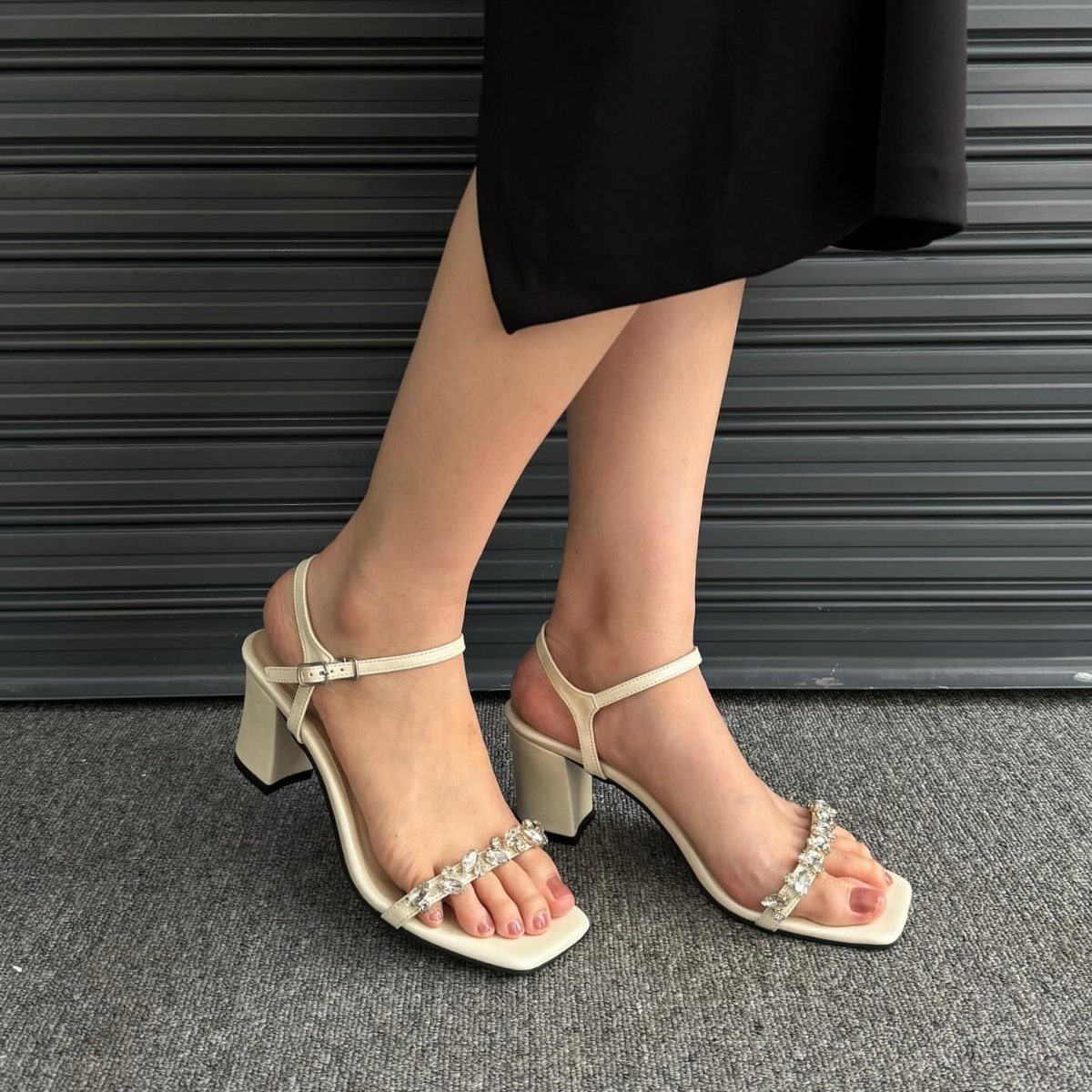 Cream block heel sandals with rhinestone straps on a person's feet.