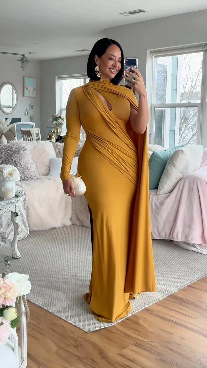 Woman in a long-sleeved mustard yellow gown with a draped cape detail.