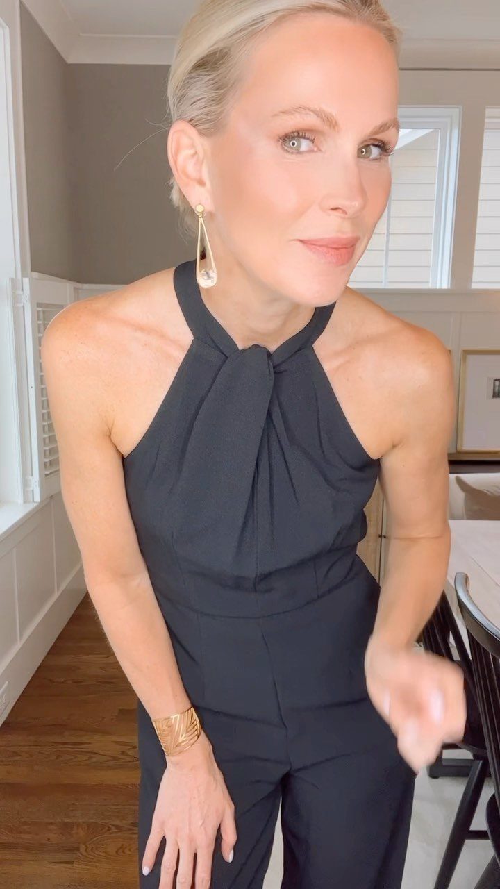 Blonde woman wearing a chic black halter-neck jumpsuit and gold accessories.