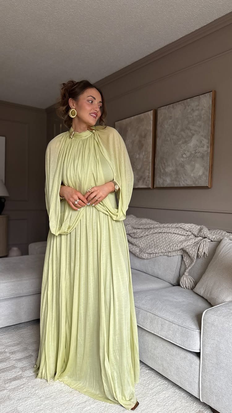 Woman wearing a long, flowing light green pleated maxi dress in a living room