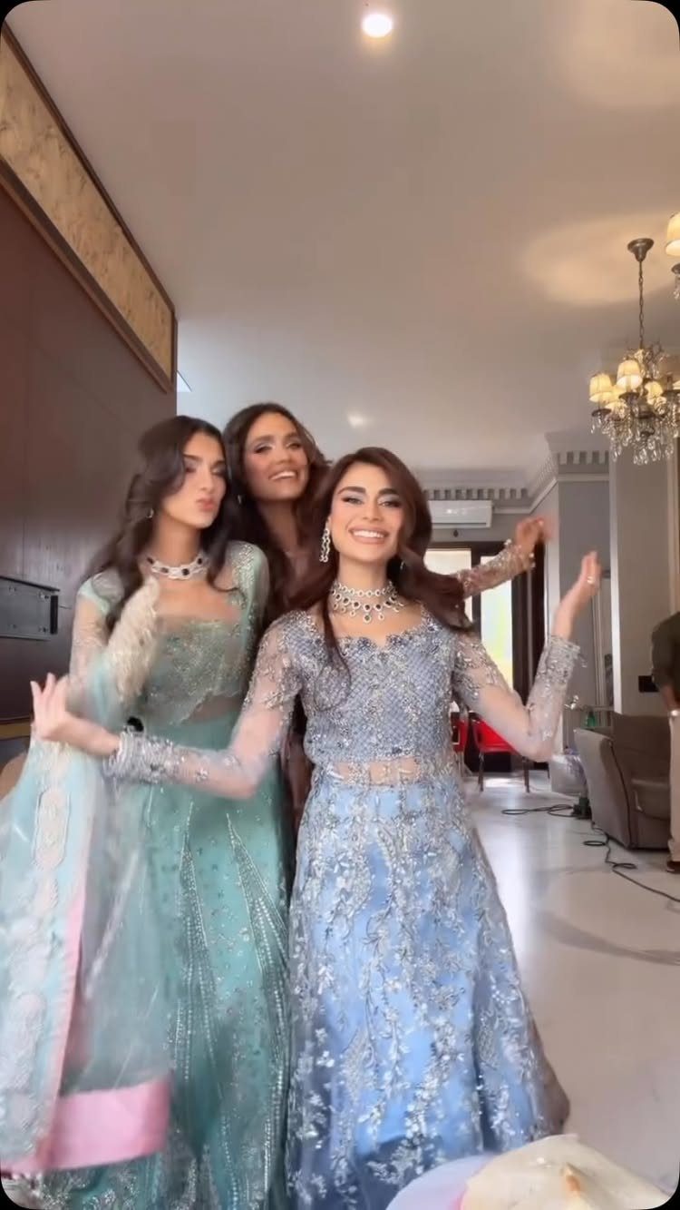 Three women wearing embellished light blue and teal South Asian formal wedding guest gowns.