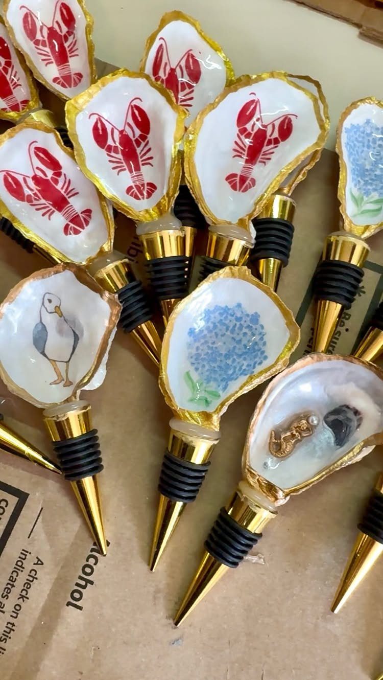 Decorative wine bottle stoppers with painted oyster shells and gold-colored metal stems.