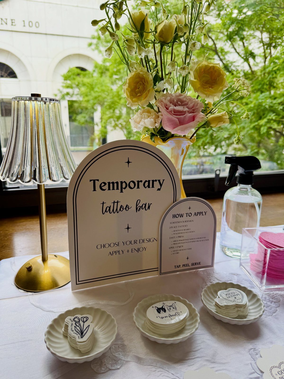 Temporary tattoo bar with designs on plates, a sign, and floral decorations.