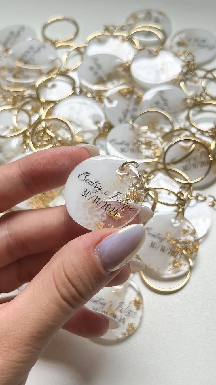 Circular white resin keychains with gold flakes and personalized text for wedding guests.