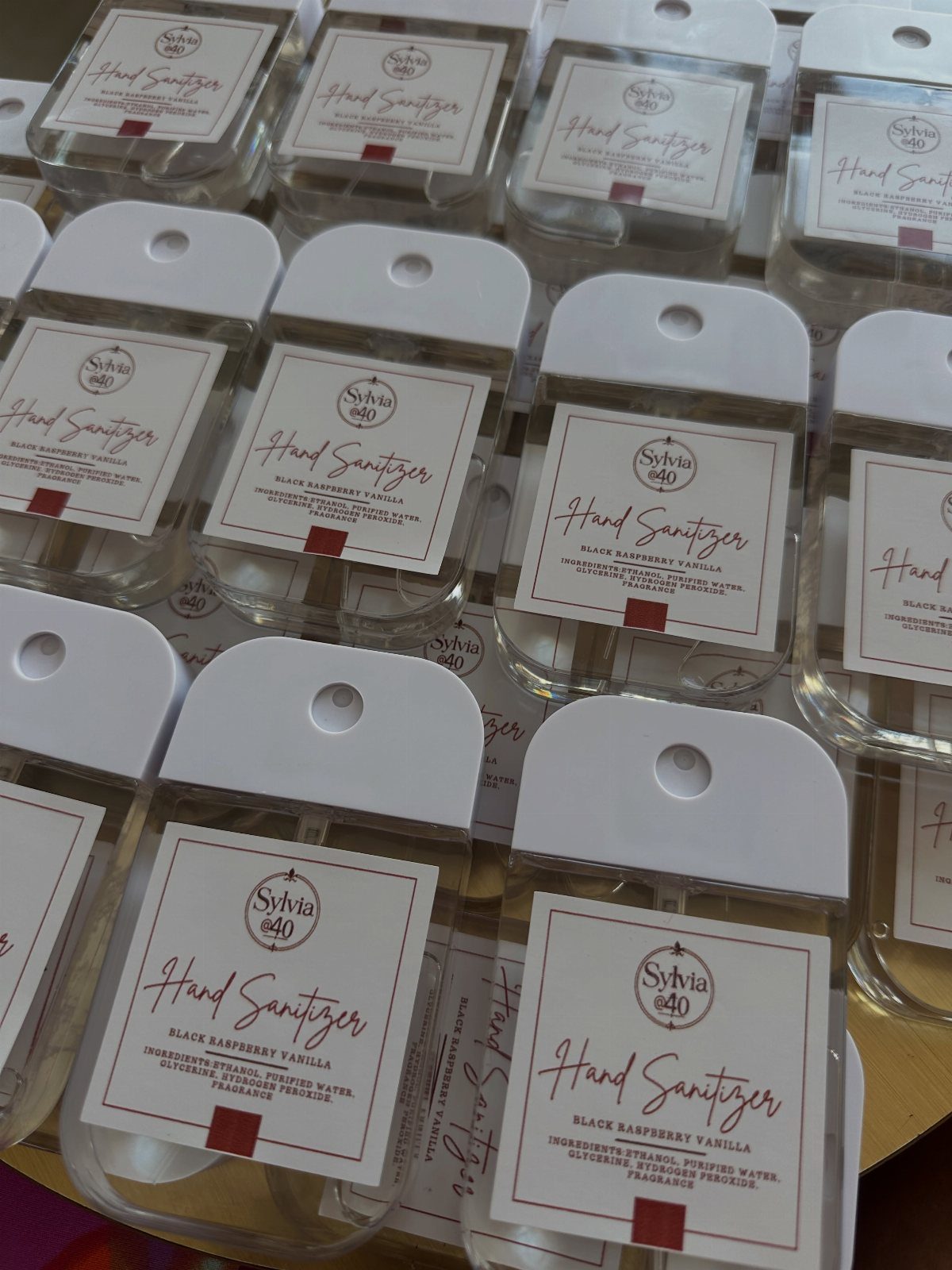 Small clear hand sanitizer bottles with personalized white labels arranged in rows.