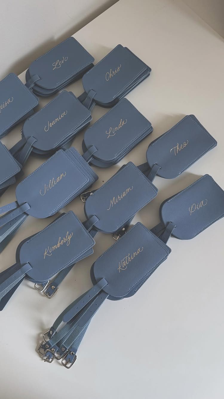 Light blue leather luggage tags with gold personalized names on a white background