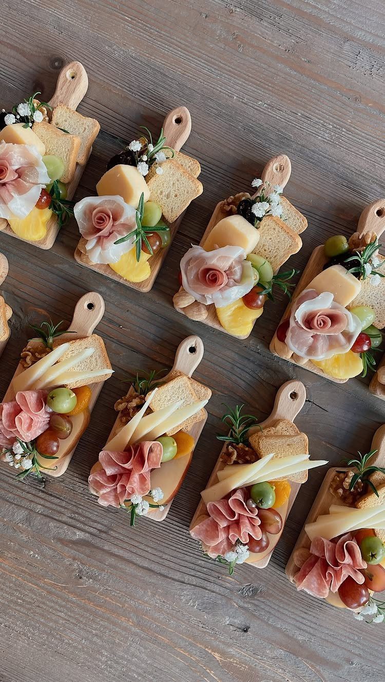 Miniature wooden cheese boards with meats, cheeses, and grapes on a wooden table