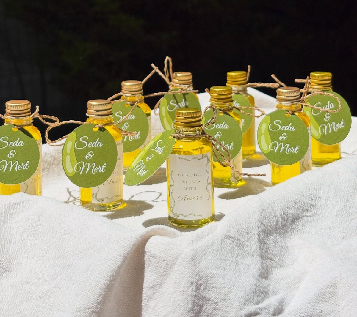 Small glass bottles of olive oil with green personalized tags on white fabric