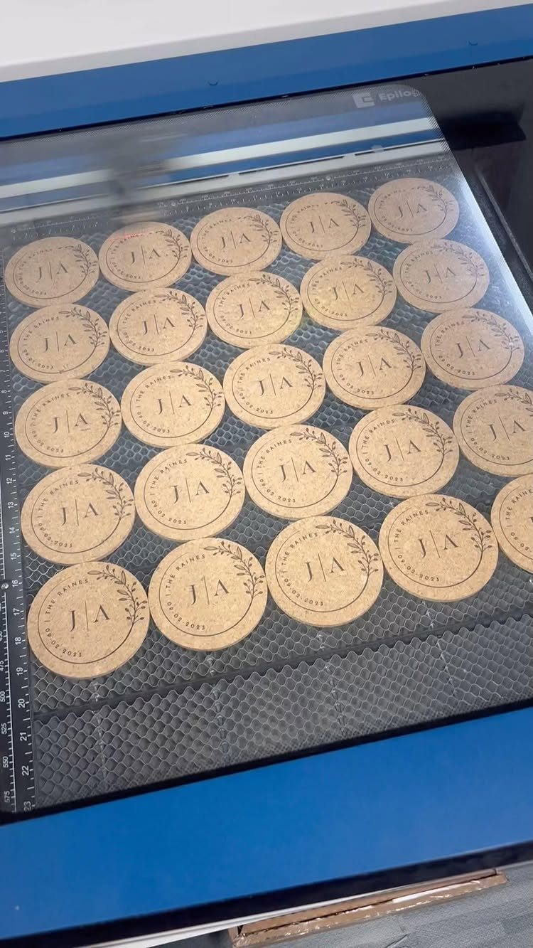 Round cork coasters with engraved initials and floral wreaths inside a laser engraver.